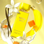 Der leuchtend gelbe Flakon von Gulf Orchid Banana Split, dynamisch inszeniert mit fließender Milch, frischer Banane, weißen Blüten und Karamellwürfeln.