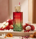 Stilvolle Präsentation des Gulf Orchid Ruby Fizz Flakons auf einem hellen Steinpodest, frisch dekoriert mit saftigen Äpfeln, Lychees und Erdbeeren.