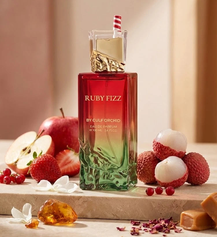 Stilvolle Präsentation des Gulf Orchid Ruby Fizz Flakons auf einem hellen Steinpodest, frisch dekoriert mit saftigen Äpfeln, Lychees und Erdbeeren.