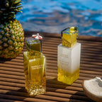Stilvolle Präsentation des Gulf Orchid Tahiti Colada Flakons auf Holzplanken vor glitzerndem, blauen Wasser, flankiert von einer ganzen Ananas und Kokosnusshälften.