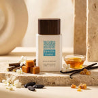 Stilvolle Präsentation des Gulf Orchid Vanilla Latte Flakons auf einem hellen Steinpodest, sanft dekoriert mit echten Vanilleschoten, süßem Karamell und weißen Blüten.