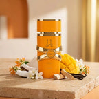 Stilvolle Präsentation des orangefarbenen Lattafa Yara Tous Flakons auf einem hellen Steinpodest, dekoriert mit frischer Mango und Kokosnuss in einer warmen, sonnigen Atmosphäre.