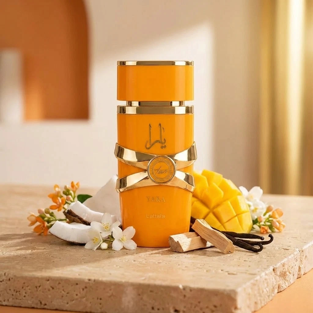 Stilvolle Präsentation des orangefarbenen Lattafa Yara Tous Flakons auf einem hellen Steinpodest, dekoriert mit frischer Mango und Kokosnuss in einer warmen, sonnigen Atmosphäre.